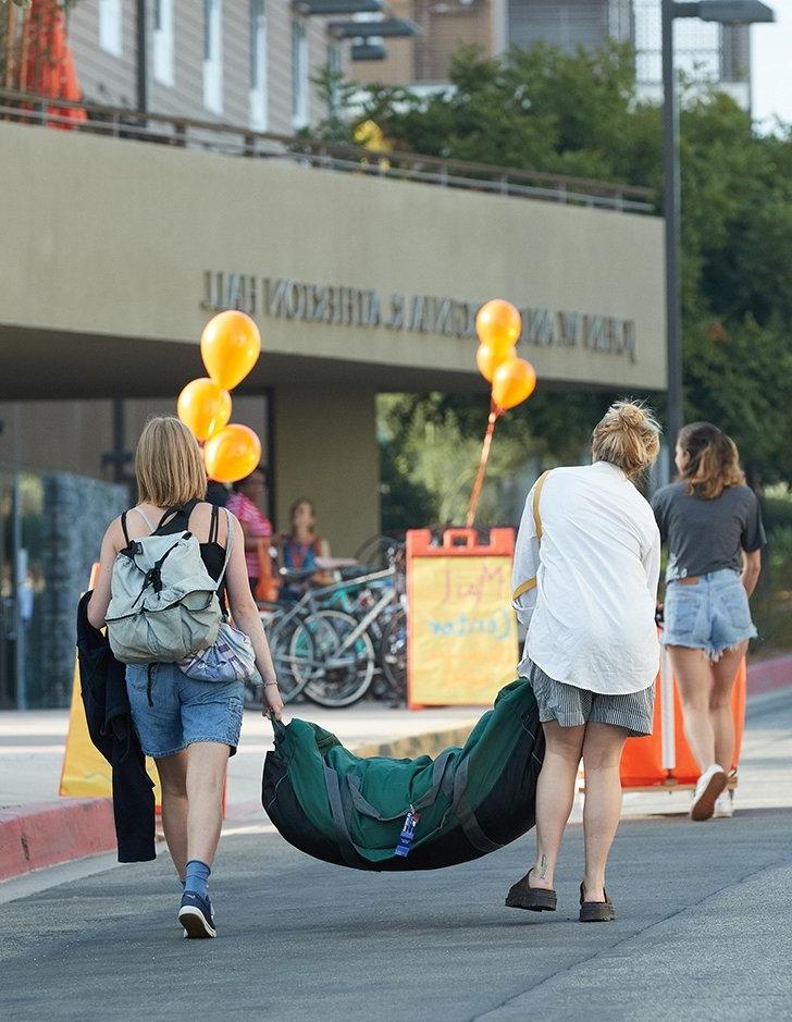 a mother and daughter move a large bag into a dorm building